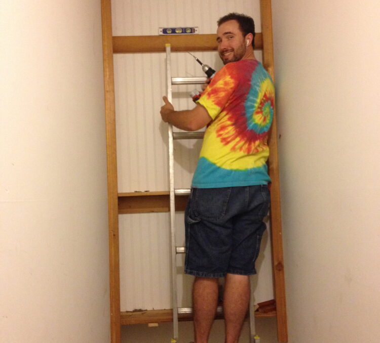 man in tie dyed shirt standing on a ladder in a stairwell