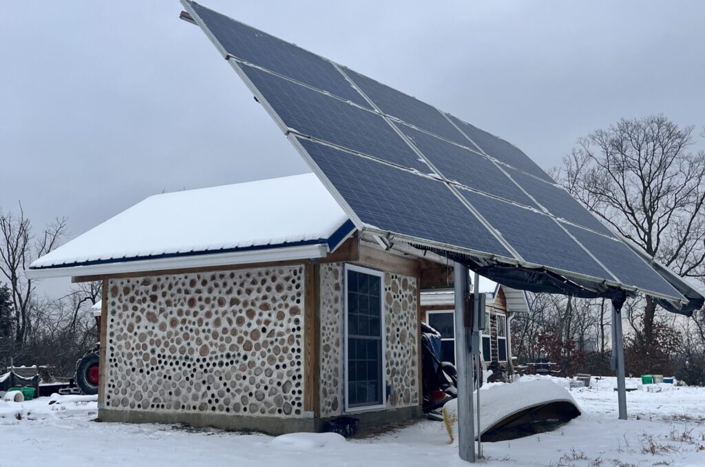 set of nine solar panels in front of a snow-covered cordwood shed