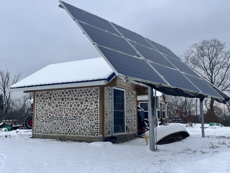 solar panels on a pole mount in front of a snow-covered cordwood shed