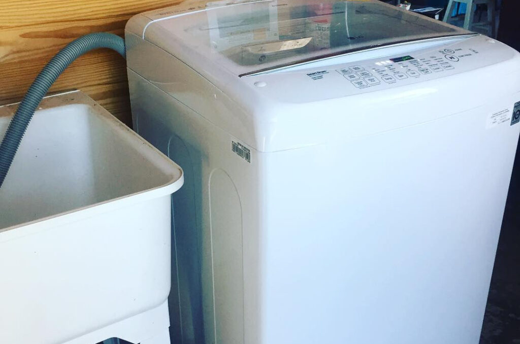 white wash tub at left with a white top load washer to its right